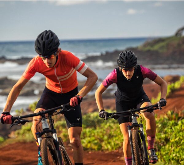 miljöbild på två mountainbikecyklister uppför i terräng med havet som bakgrund